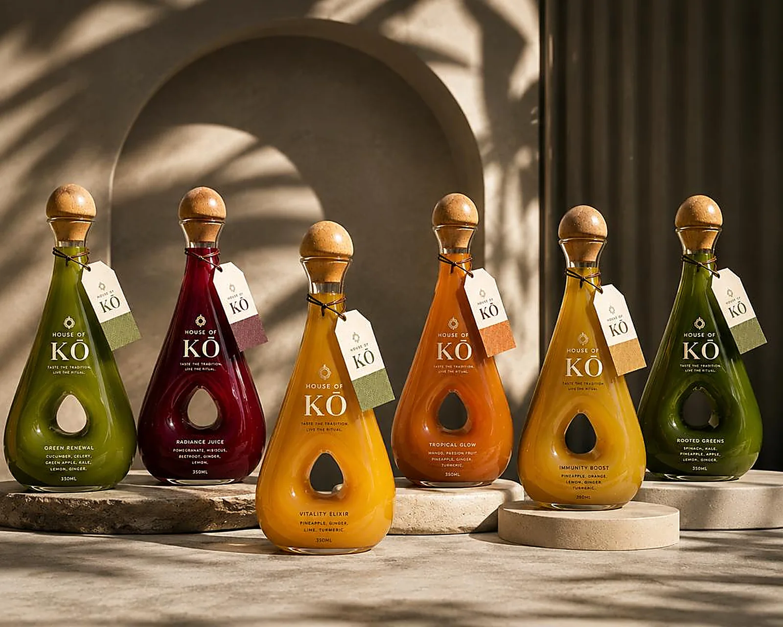 Six House of KŌ cold-pressed juices — Green Renewal, Radiance, Vitality Elixir, Tropical Glow, Immunity Boost and Rooted Greens — on stone plinths